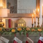 Cozy cottage Christmas mantel styled with thrifted holiday decor, including brass deer figurines, greenery garland, fairy lights, and vintage picture frames for a charming, collected Christmas look.