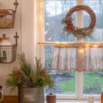 A cozy vintage kitchen shelf decorated for Christmas with old cookbooks, ceramic Santa mugs, stacked ironstone, and a red-ribbon wreath.